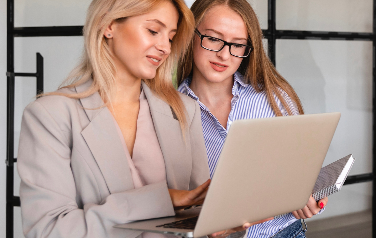Build confidence and achieve career success | Vono Creative | Image shows two women standing in an office, looking at an open laptop.